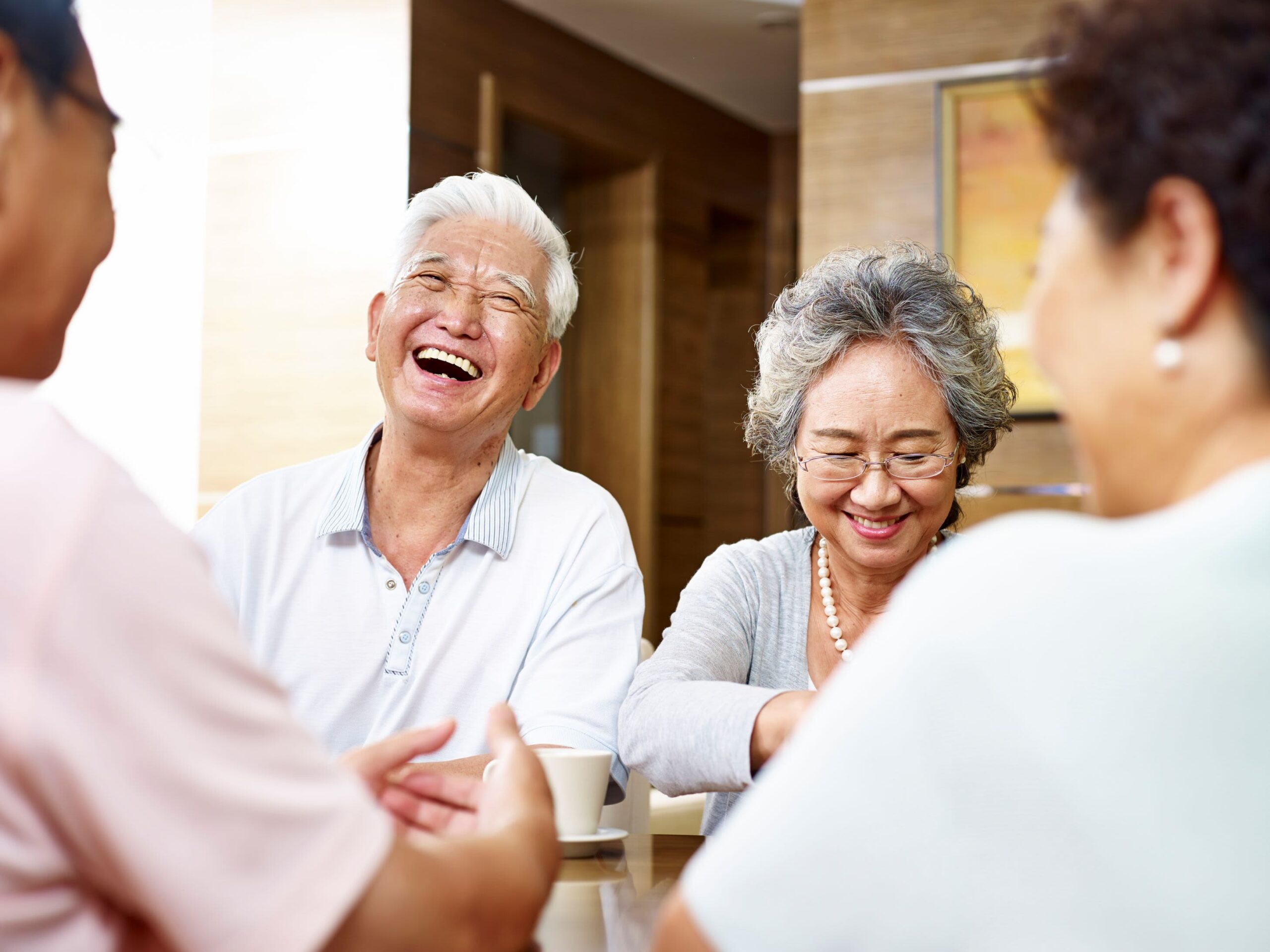 Four older adults laughing together over coffee